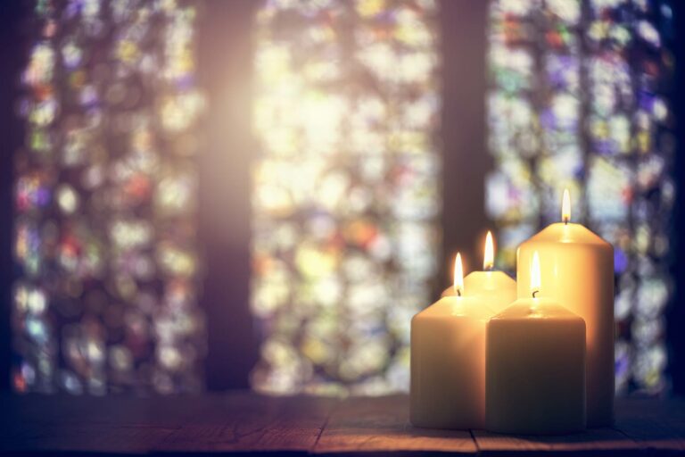Three candles in front of a stained glass window.