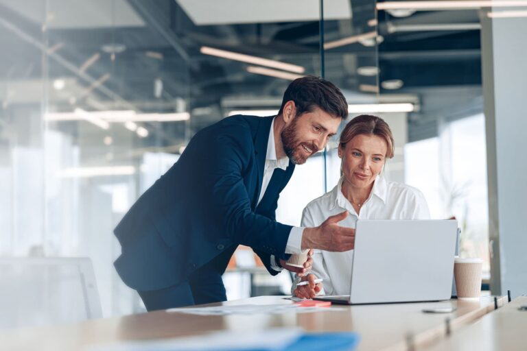 A man and a woman in a business setting looking at a laptop on a desk