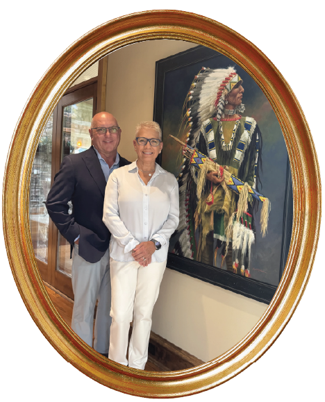 This picture shows CAPTRUST Financial Advisor Mike Molewski and his wife standing beside one of the paintings they own. In it, a Native American man in a long headdress stares into the distance.